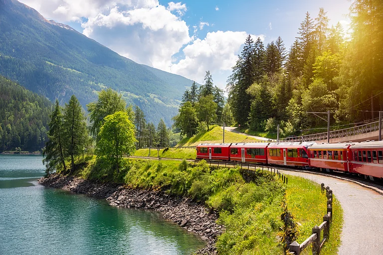 Red train moving along lake in beautiful mountain landscape in Switzerland - Shutterstock