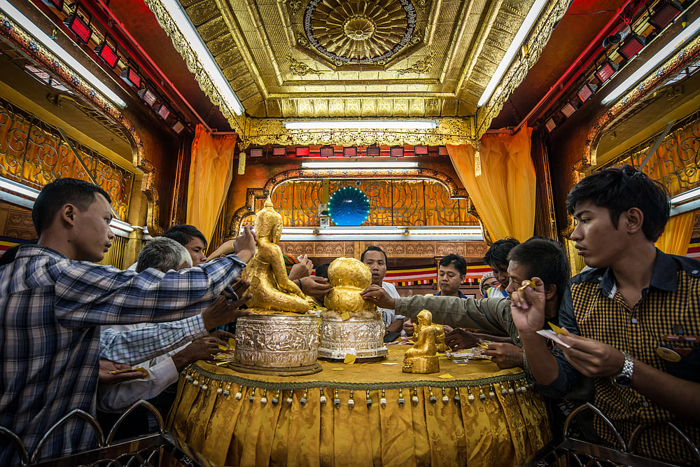 People sticking gold leaf on Buddha figurines
