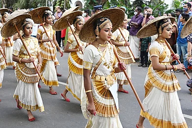 AjayTvm/Shutterstock : Dancers in traditional kasavu dress and palm leaf umbrells during Onam celebrations in Trivandrum, Kerala