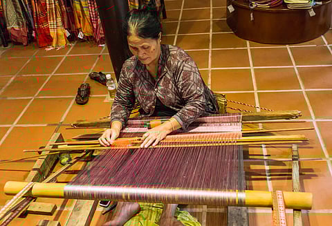 A Champa woman uses an antique wooden loom to weave silk at the Hội An Silk Village