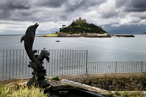 St Michael's Mount under cloudy skies with submerged walkway to Marazion from The Square with Two Dolphins sculpture Marazion, Cornwall, UK