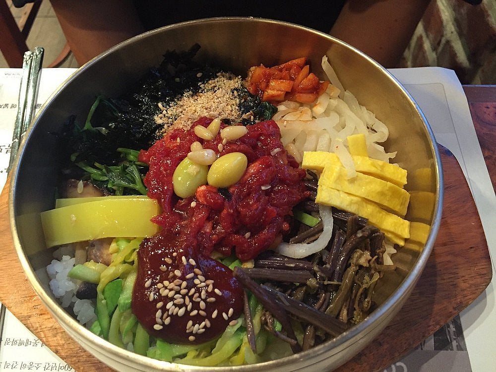 Hangugjibs bibimbap is served in a brass bowl and filled with raw beef, vegetables and nuts