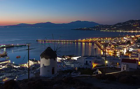 The windmills of Mykonos silhouetted against the night lights of the town