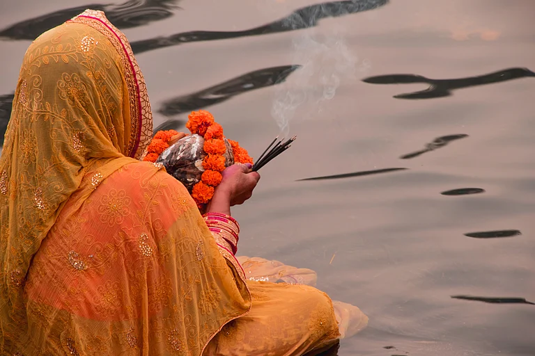 A lady performs Chhath puja by a river - Shutterstock