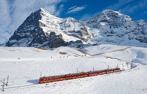 A cogwheel train travels on the railway from Jungfraujoch to Kleine Scheidegg on the snowy hillside in Bernese Highlands, Switzerland