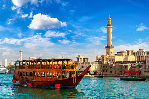 Old traditional wooden ship and Grand Bur Dubai Masjid Mosque on the bay Creek in Dubai, United Arab Emirates