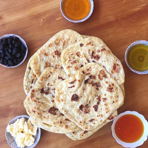 A platter of msamman served with jam, olive oil, honey, butter, and olives.
