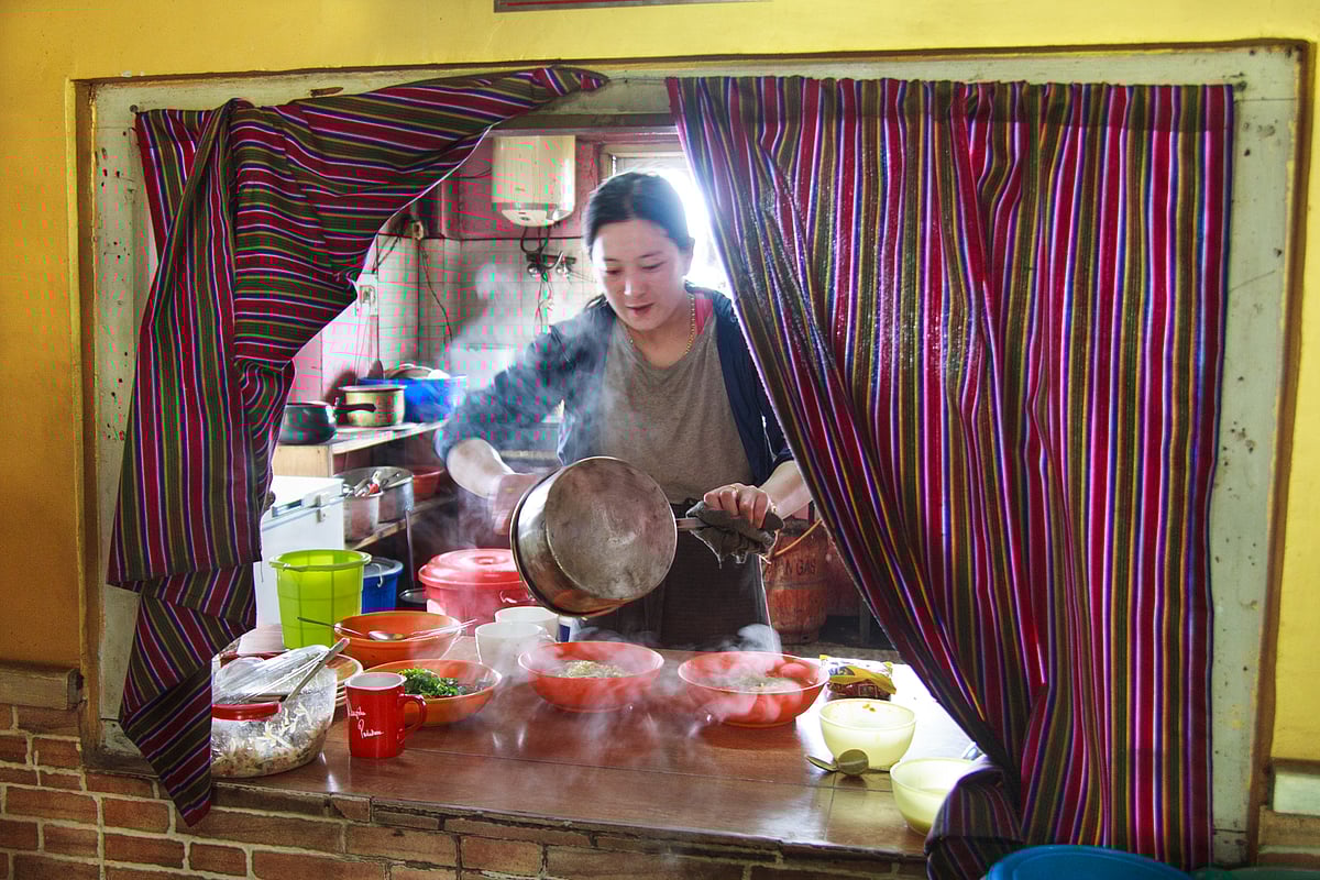 A Bhutanese lady serves a steaming bowl of traditional thukpa from her home-run restaurant. The warm, savoury soup is the perfect comfort food to counter the chilly weather