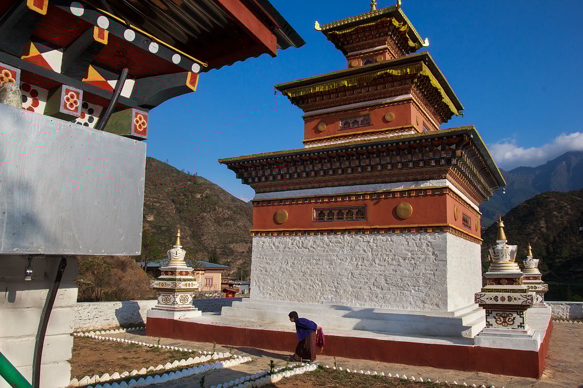 Near Paro, this small shrine stands in harmony against the backdrop of the surrounding hills, its vibrant Bhutanese architecture with earthy hues standing out in the soft sunlight. An elderly woman bows in prayer
