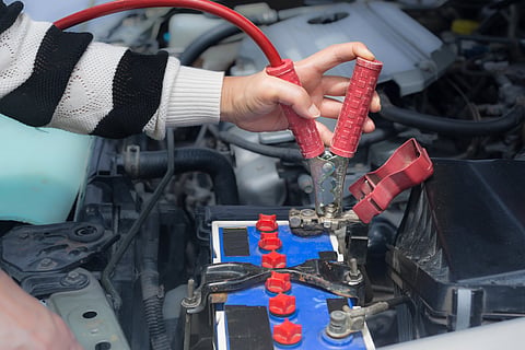 A woman attaching jumper cables to a car's battery