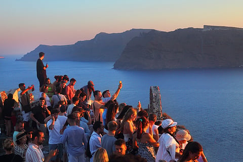 A crowd of tourists see the sunset from Oia village in Santorini