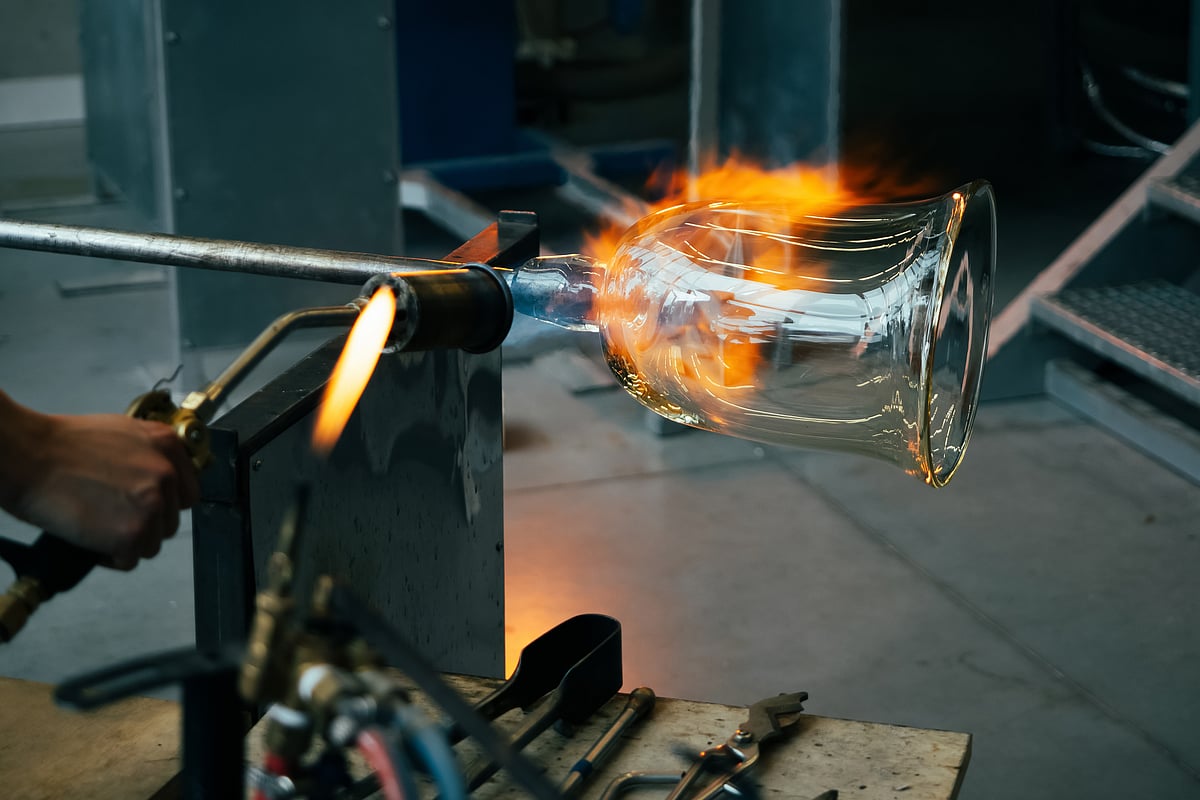 An artisan shapes hot molten glass at a glass-making factory.
