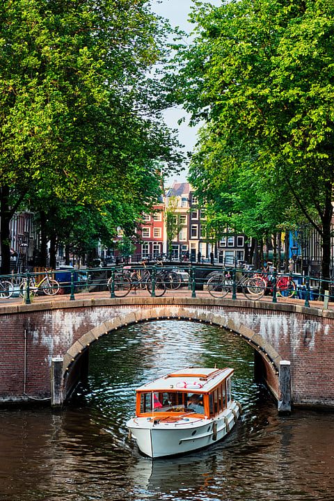 A view of canal with boat passing under bridge and old houses, Amsterdam
