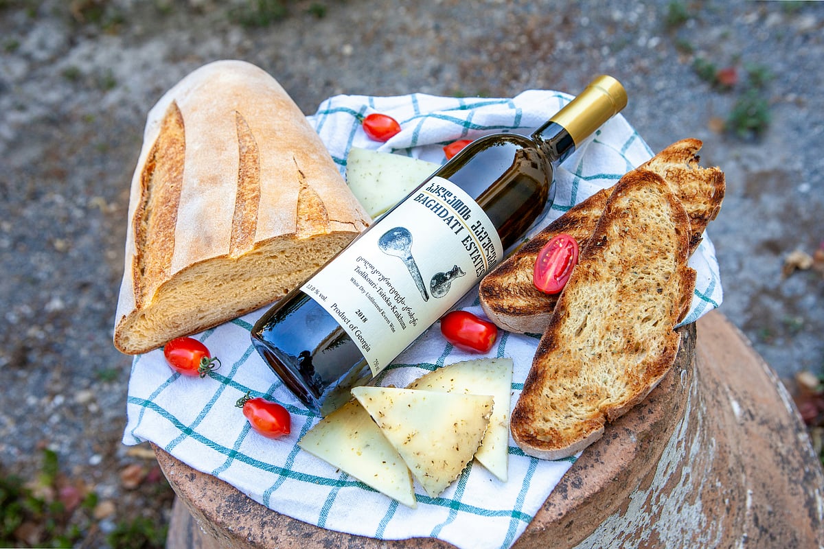 Photo by ALEXANDRA TORRO on Unsplash : A bottle of Georgian natural wine with fresh bread, cheese, and cherry tomatoes