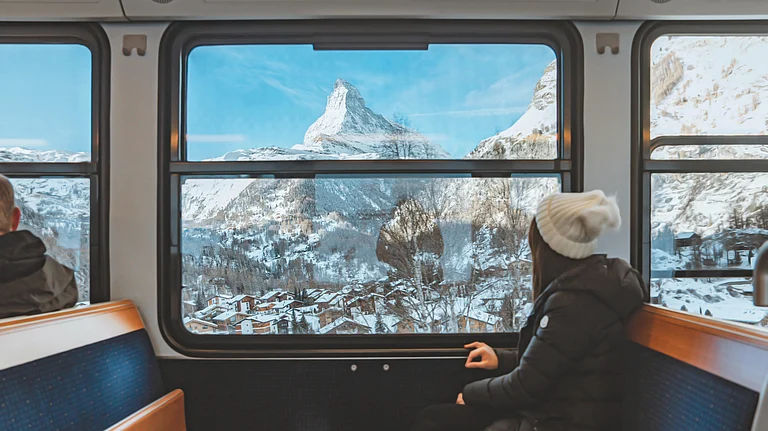 A young woman gazes out the window while travelling through the Swiss Alps, with the Matterhorn rising majestically in the winter background - Shutterstock
