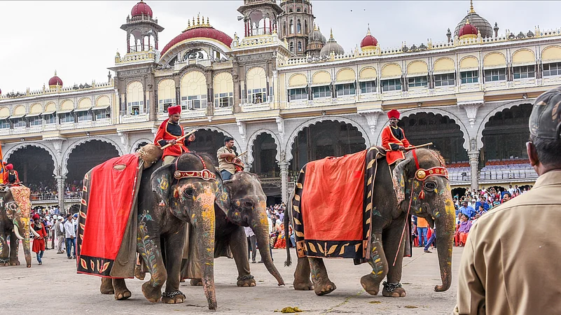 Men riding on decorated elephants with umbrella at Mysore Maharajas Palace as people watch the procession on Dussehra