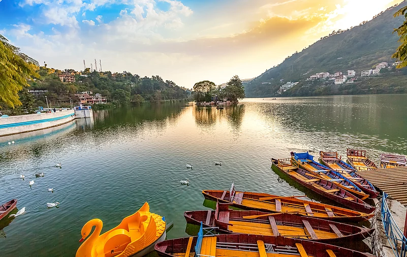 A serene view of Bhimtal Lake at sunset, with wooden boats floating on calm waters