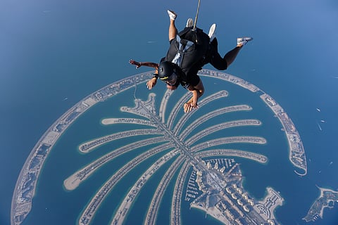 Skydivers glide over Dubai’s iconic Palm Jumeirah on a clear, sunny day