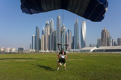 Tandem skydivers descend by parachute with Dubai’s skyline in the backdrop