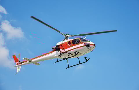 A helicopter with a mounted camera soars against a clear blue sky