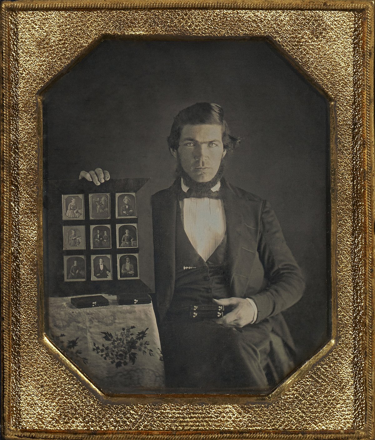 Daguerreotype portrait of a daguerreotypist displaying daguerreotypes and cases pictured in an airtight frame, 1845