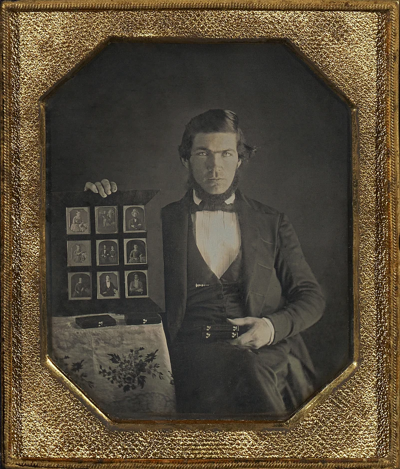 Daguerreotype portrait of a daguerreotypist displaying daguerreotypes and cases pictured in an airtight frame, 1845