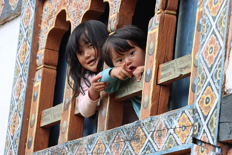 Two curious children peek from a wooden window, capturing the gentle charm of daily life in Paro, Bhutan