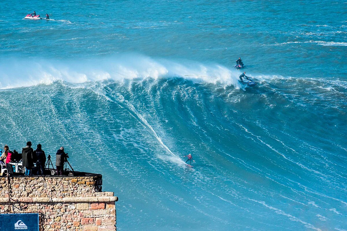 Surfing the high waves at Praia do Norte beach in Nazaré, Portugal