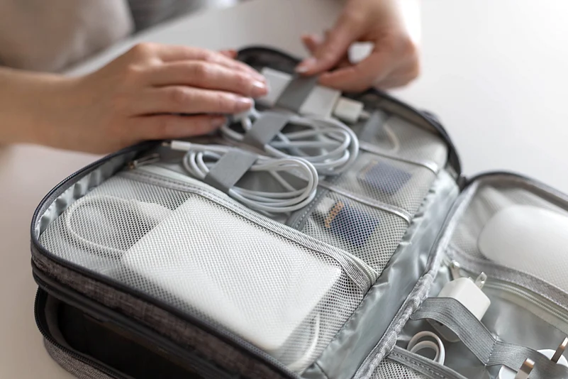 A traveller organises and packs cables and travel tech in a pouch