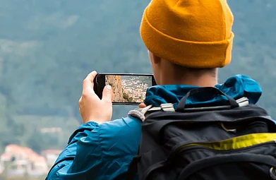 Shutterstock : A traveller photographs a mountain village on his phone during a hike