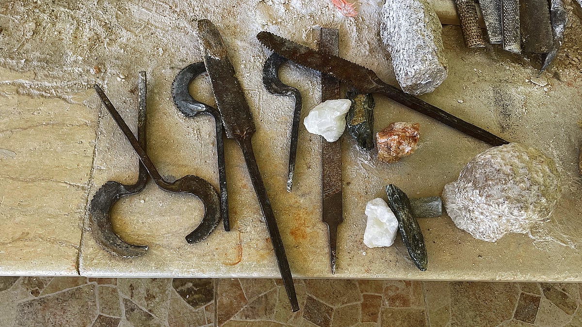 Traditional Egyptian alabaster carving tools, including chisels (izmīl), curved blades (mangal naḥt), files (mibrad), and raw alabaster stone, used by craftsmen