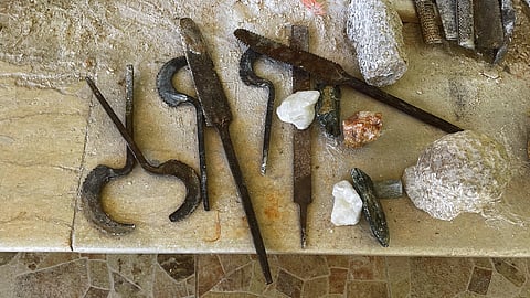 Traditional Egyptian alabaster carving tools, including chisels (izmīl), curved blades (mangal naḥt), files (mibrad), and raw alabaster stone, used by craftsmen