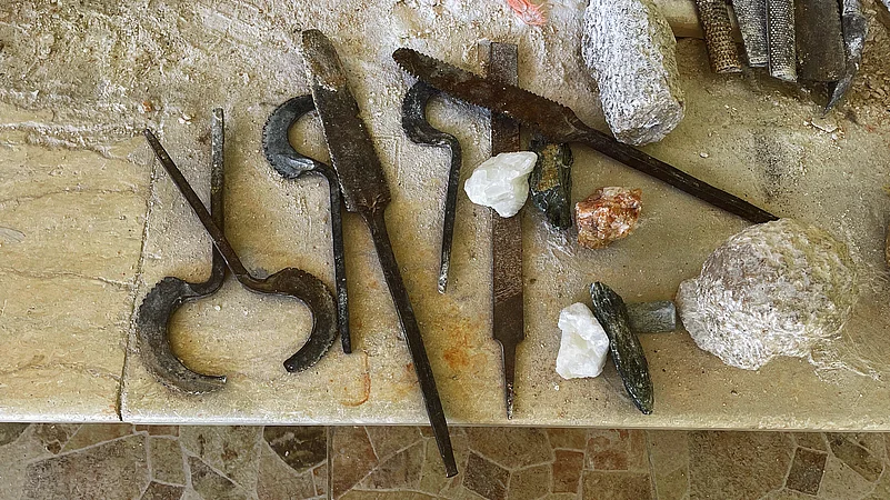 Traditional Egyptian alabaster carving tools, including chisels (izmīl), curved blades (mangal naḥt), files (mibrad), and raw alabaster stone, used by craftsmen