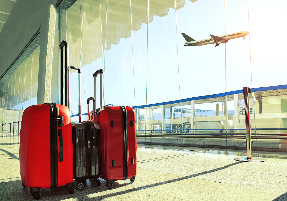 Luggage stacked at an airport terminal as flight departs overhead
