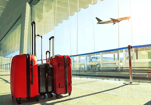 Luggage stacked at an airport terminal as flight departs overhead