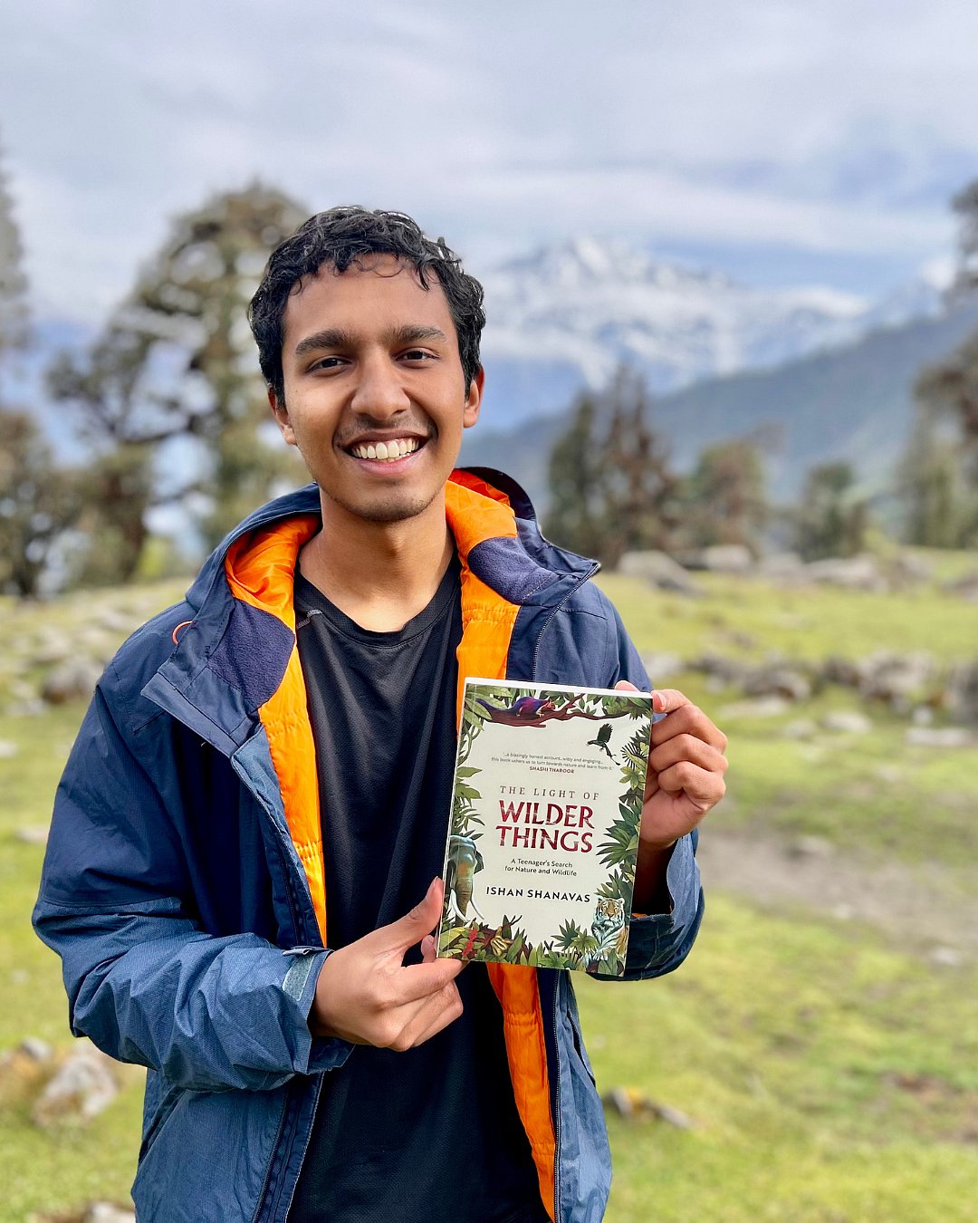 Ishan Shanavas holds his book, The Light of Wilder Things, in a natural setting that reflects the works focus on nature and wildlife. in human words