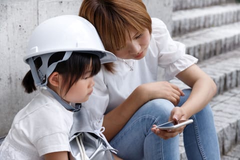 Mother and child checking updates during a disaster, wearing safety helmets (Representative image)