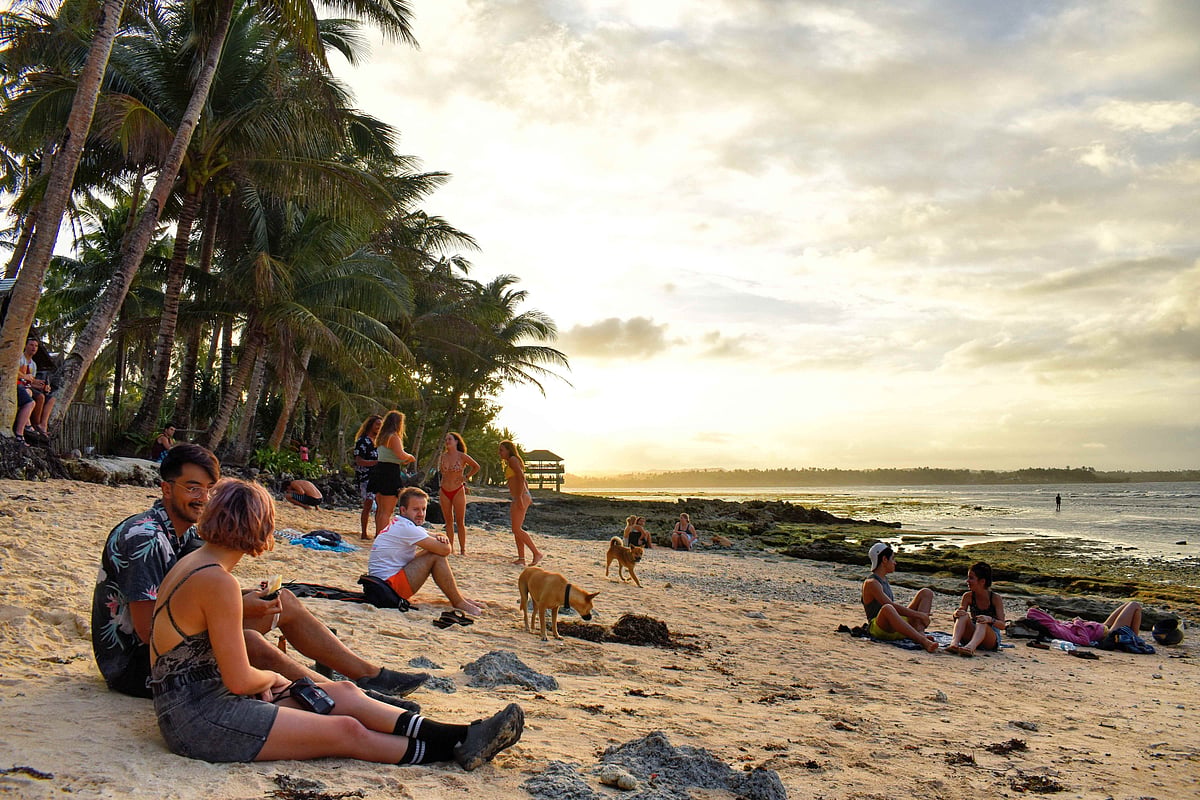 People relaxing by the shore at Cloud 9, watching surfers ride the waves