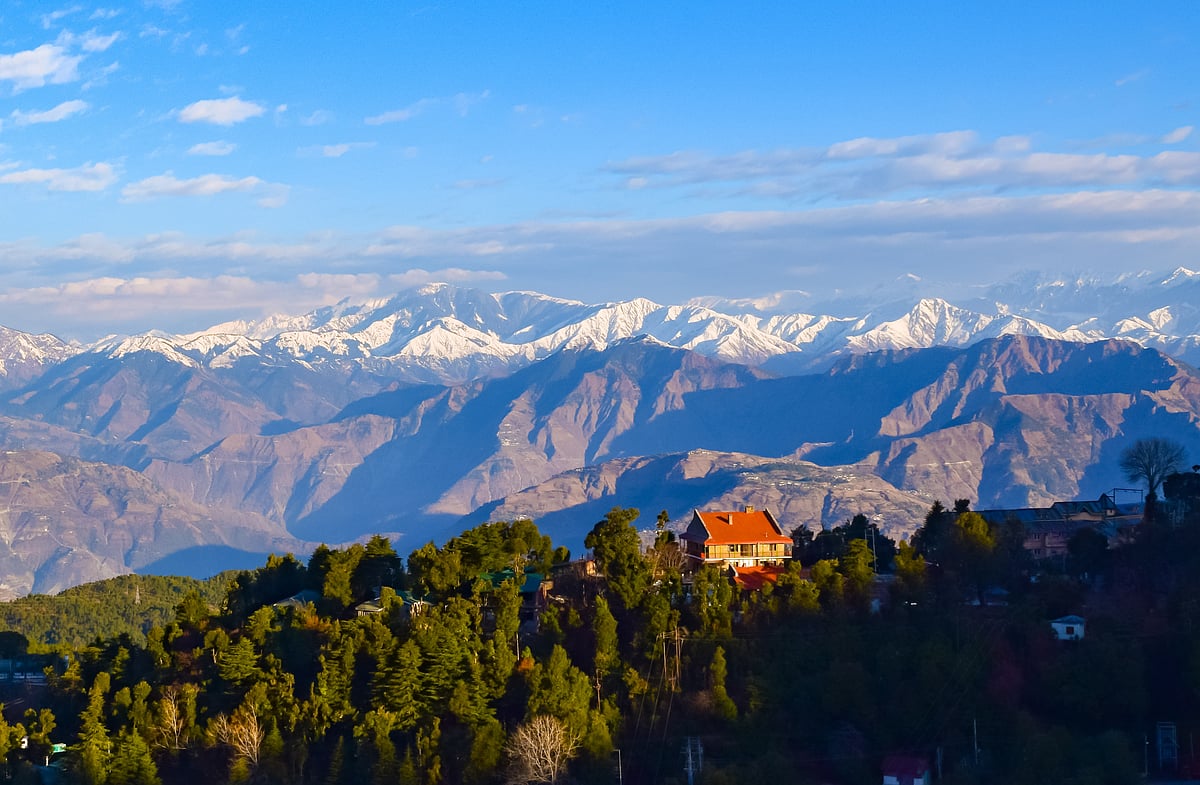 A view of snow-capped Himalayan peaks behind the forested hills of Khajjiar, Himachal Pradesh