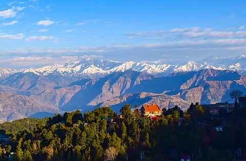 A view of snow-capped Himalayan peaks behind the forested hills of Khajjiar, Himachal Pradesh