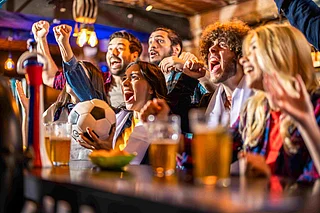 Shutterstock : Fans cheer for their team while watching a football match at a sports bar