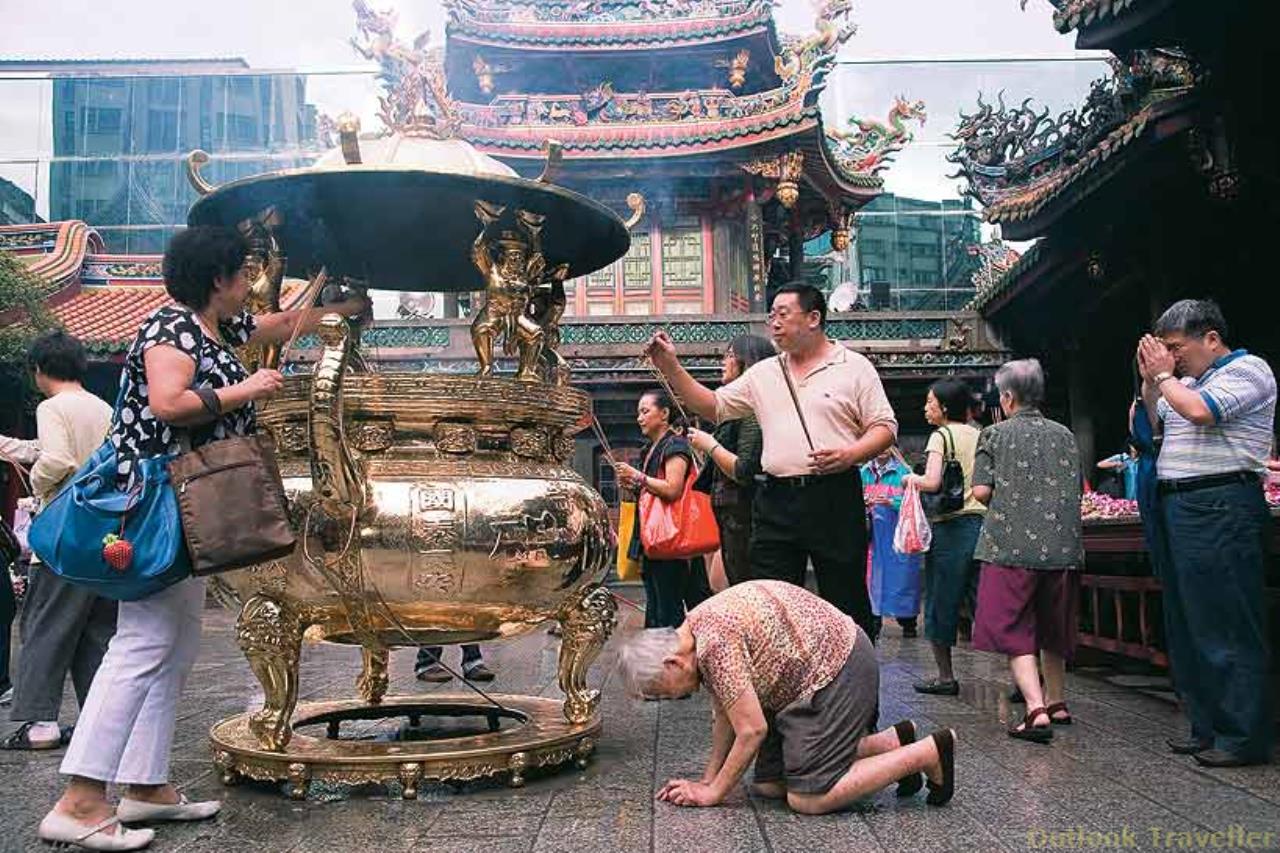 An elderly lady bows at the Long Shan temple as worshippers move around her