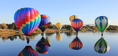 A bunch of hot air balloons gliding over a lake