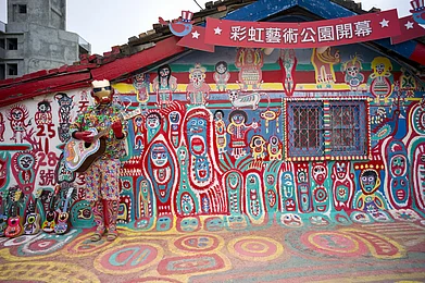 A street performer plays guitar in front of the colorful graffiti painted in the Rainbow Village of Taiwan. Photo Credit Gary Yim / Shuterstock