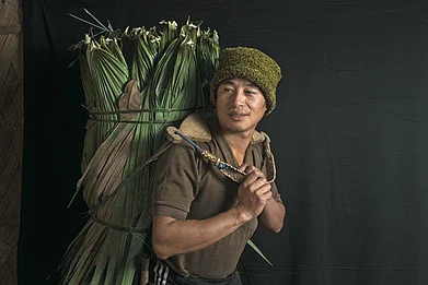 A Lisu man carrying leaves from the forest to help construct a neighbours house in Nibudi.