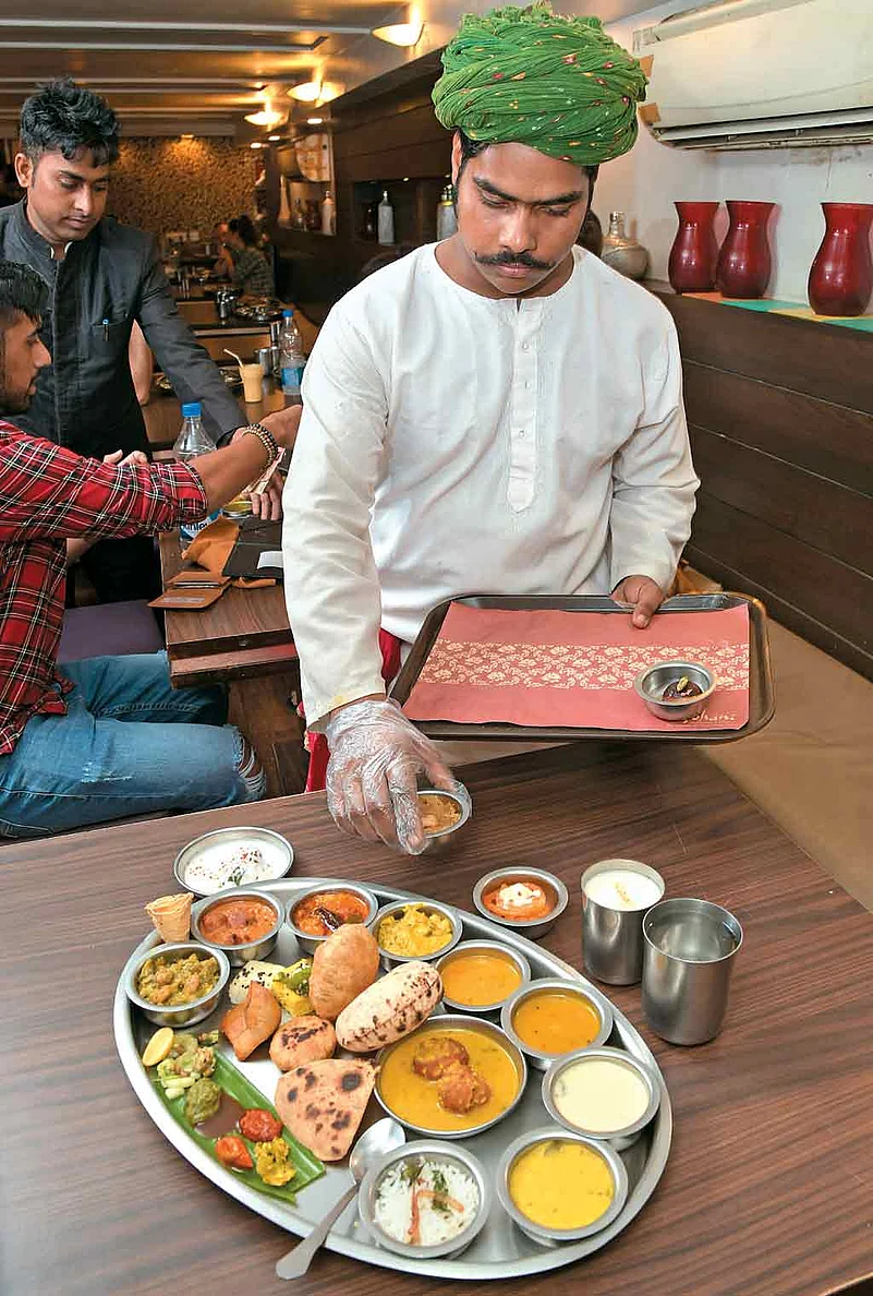 A server setting up a Gujarati thali at a restaurant