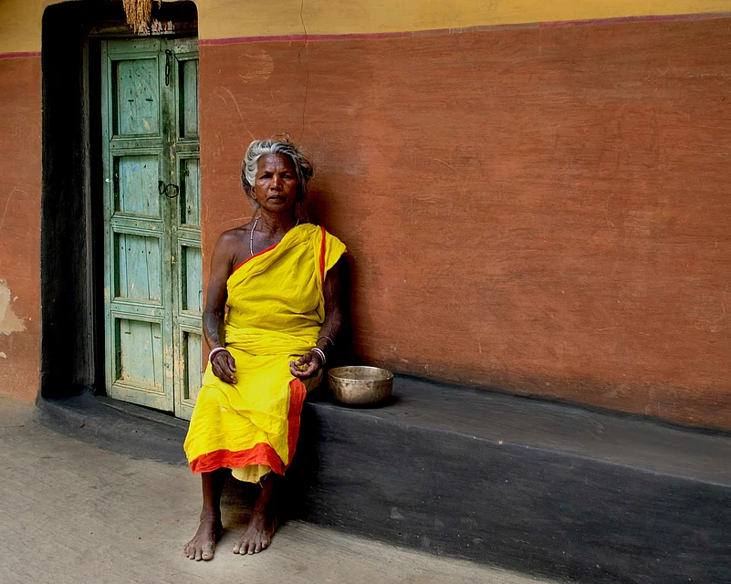 An elderly woman belonging to the Santhal tribe outside her home