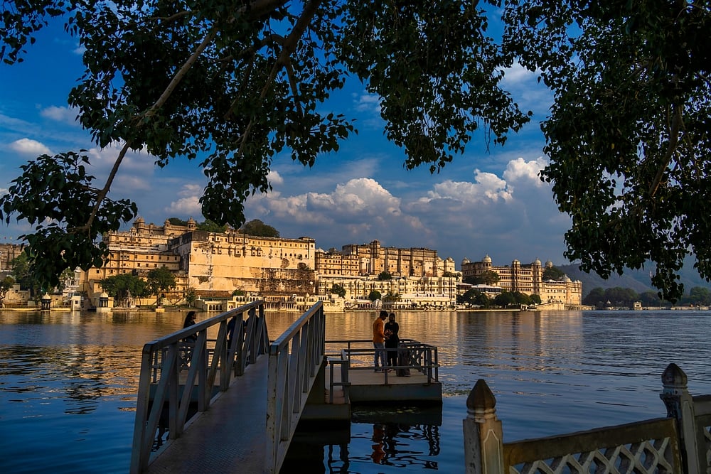 Ambrai Ghat, situated along the eastern banks of Lake Pichola in Udaipur, is a picturesque waterfront promenade celebrated for its panoramic views and cultural allure. Facing the majestic City Palace and Jag Mandir, the ghat offers an enchanting vista of Udaipurs architectural splendour against the backdrop of the Aravalli hills. Locals and tourists frequent Ambrai Ghat to witness stunning sunsets over Lake Pichola. The ghats tranquillity, complemented by the glittering lights of the City Palace reflecting on the water, makes it a romantic destination. Additionally, the ghat is home to various eateries, providing a delightful ambience for visitors.