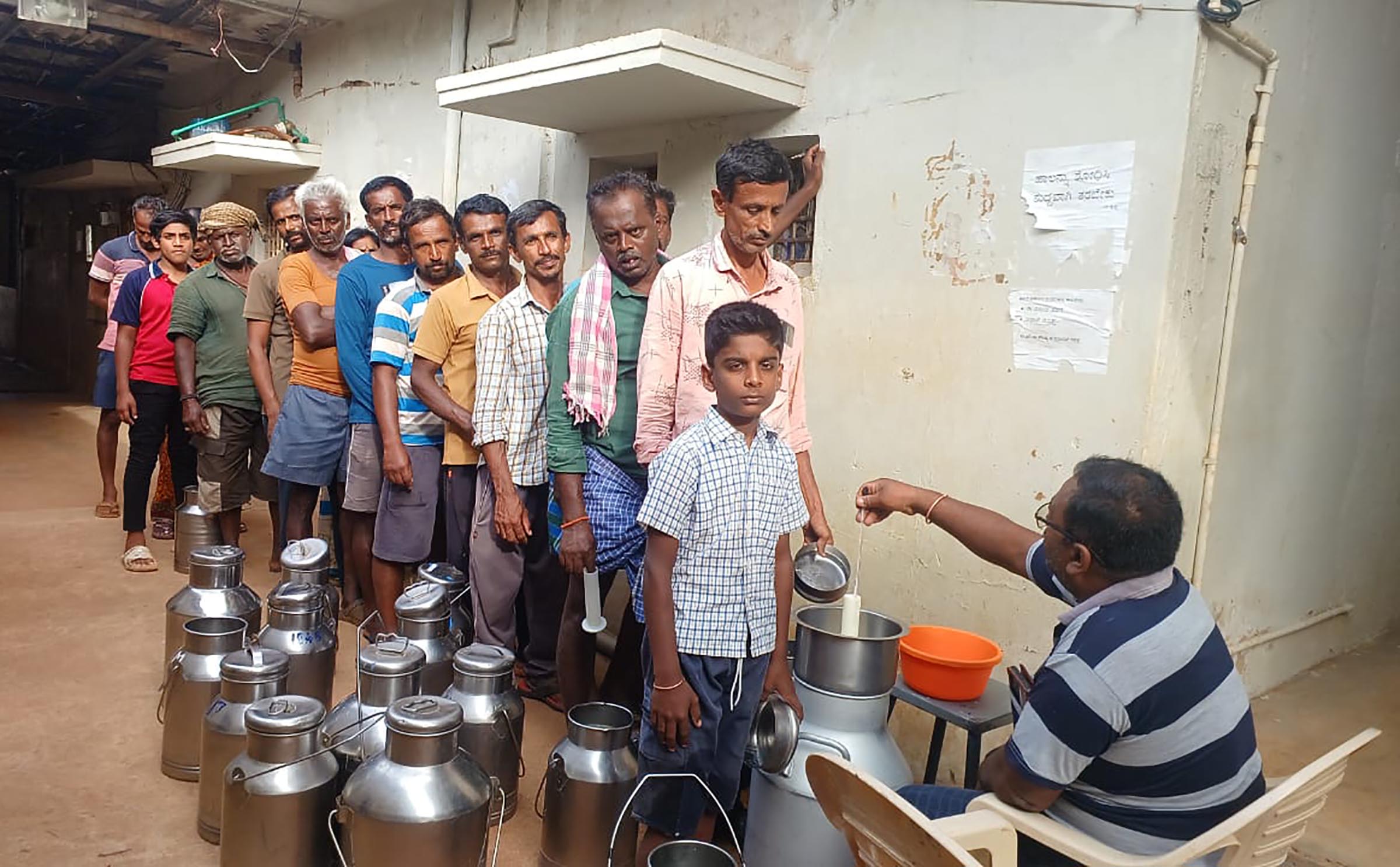 ಮಳಮಾಚನಹಳ್ಳಿ ಡೇರಿ ಬಳಿ ಹಾಲು ಹಾಕಲು ಸಾಲಲ್ಲಿ ನಿಂತ ಹೈನುಗಾರರು