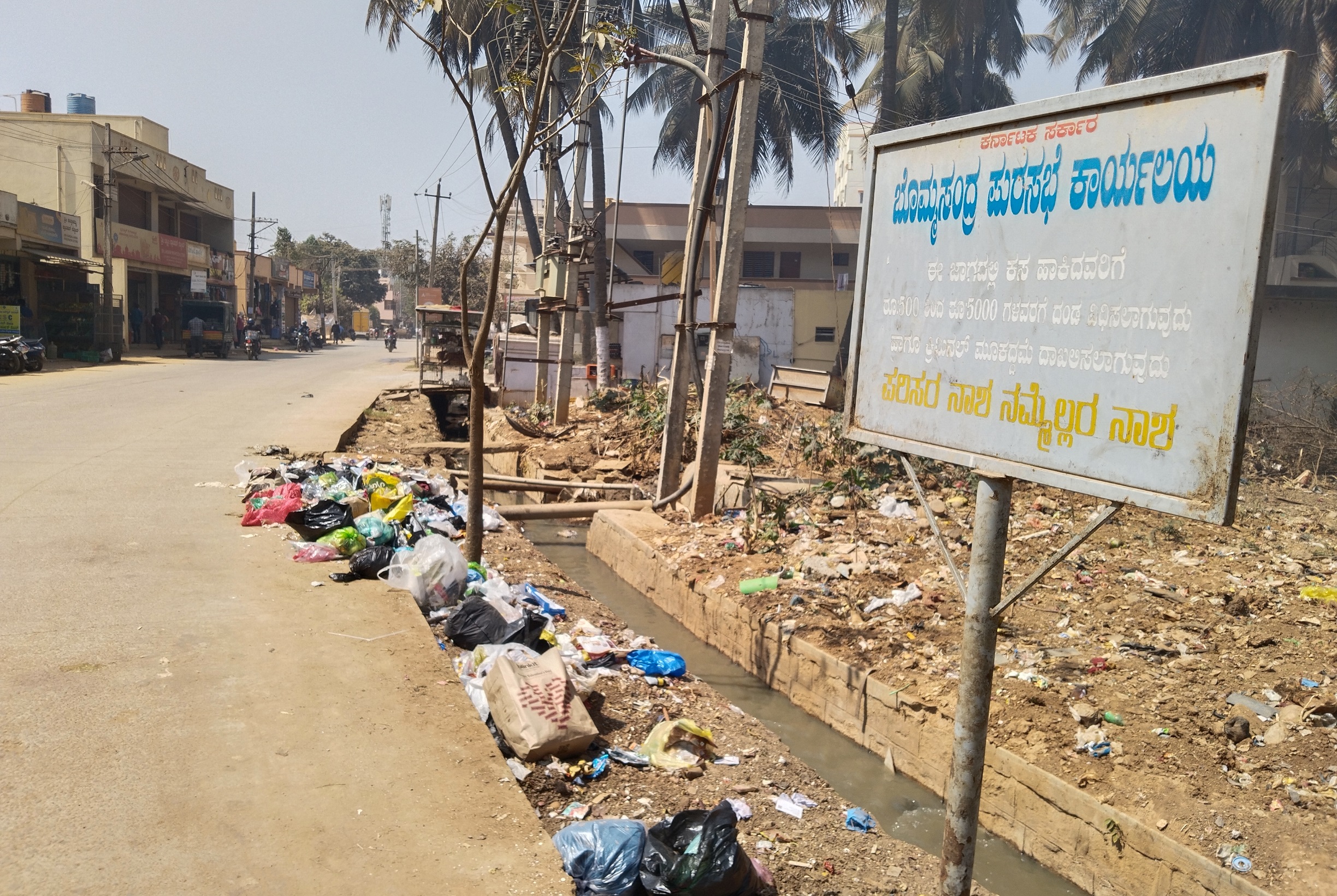 ಇಲ್ಲಿ ಕಸ ಹಾಕಿದರೆ ದಂಡ ವಿಧಿಸಲಾಗುವುದು ಎಂಬ ಫಲಕದ ನಡುವೆಯೂ ಕಸ ಬಿದ್ದಿರುವುದು